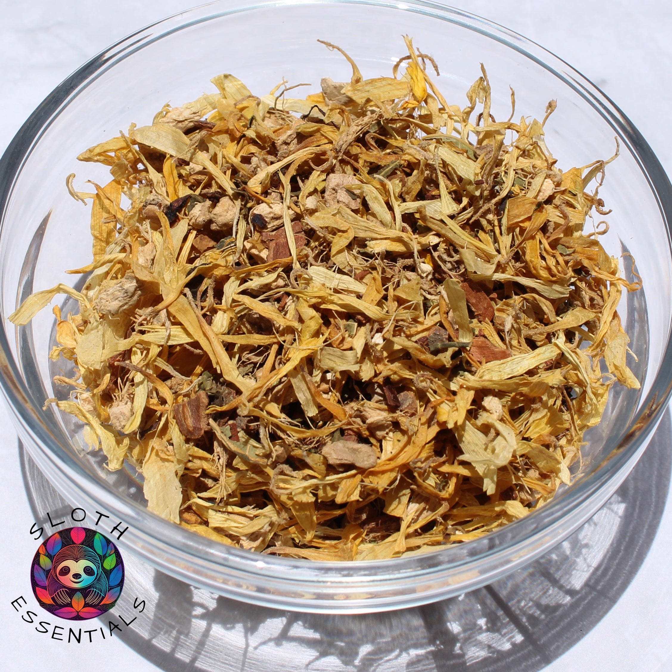 Close-up of Ginger Papaya Leaf Tea blend in a glass bowl, showcasing ginger, papaya leaf, cinnamon, orange peel, honey bush leaves, and calendula petals.