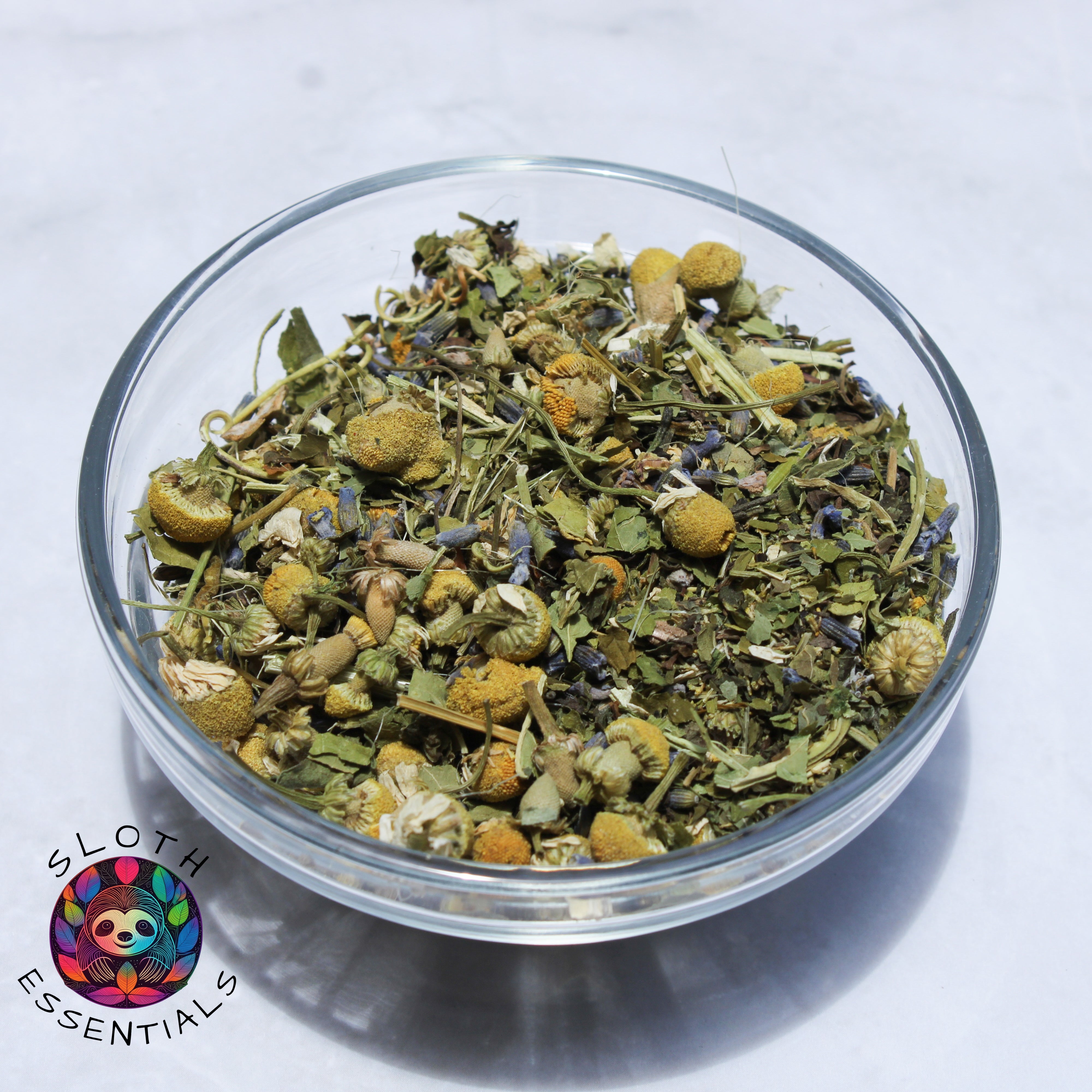 Close-up of Sloth Snooze Blend ingredients in a glass bowl, showcasing chamomile, lavender, passionflower, lemon balm, and skullcap for a soothing tea experience.